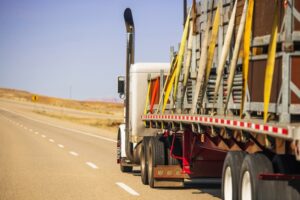 American semi truck trailer carrying oversize cargo securely fastened with lashing straps, emphasizing heavy-duty transportation safety.