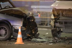 Damaged in heavy car accident vehicles after collision on city street crash site at night.