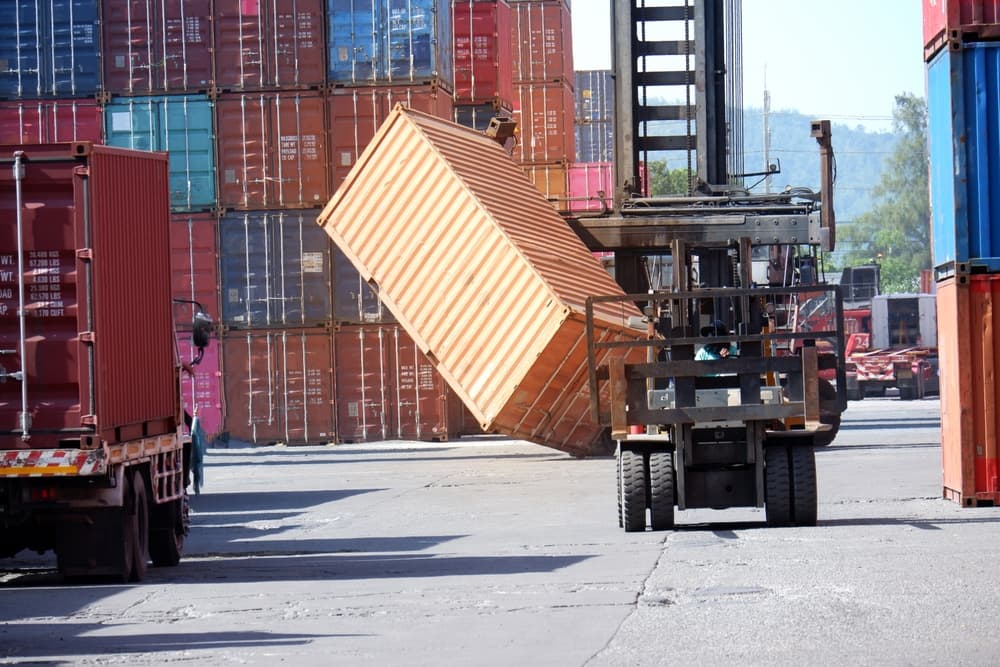 Container forklifts handling damaged goods in a yard or wharf, with a focus on high insurance coverage for the cargo.